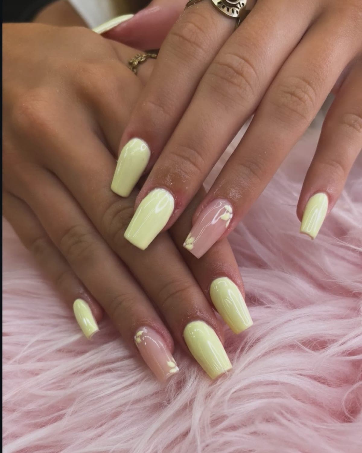 Uñas largas cuadradas en amarillo pastel con dos uñas nude decoradas con flores en relieve