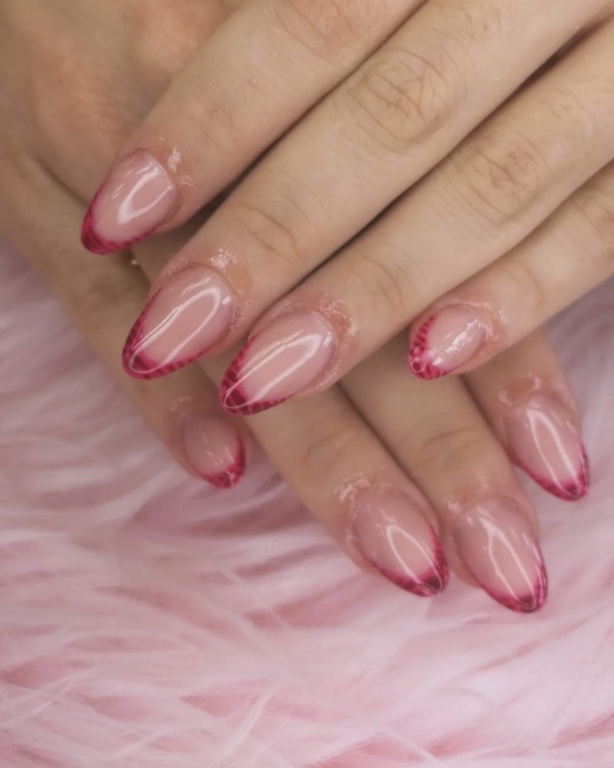 Uñas almendradas con francesa en burdeos y borde difuminado sobre pelo rosa